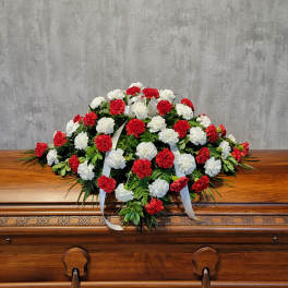 Red and white carnation casket spray with white ribbon on a wooden casket