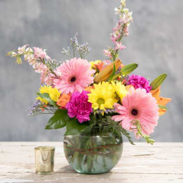 Colorful mixed bouquet in a round glass vase with a small candle nearby