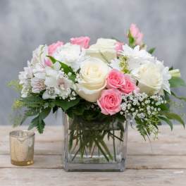 Pink and white roses arranged in a clear square vase