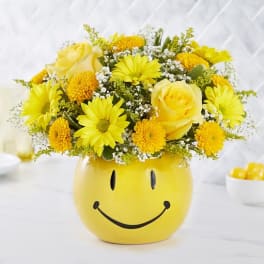 Yellow flower arrangement in a smiley-face ceramic pot