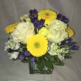 Bouquet of white roses, yellow daisies, and purple flowers in a glass vase