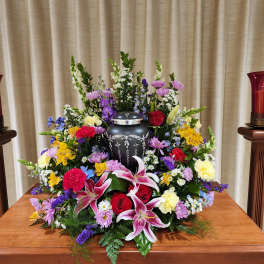Large funeral flower arrangement with lilies, roses, and mixed blooms around an urn