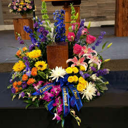 Large colorful funeral floral arrangement around a wooden urn