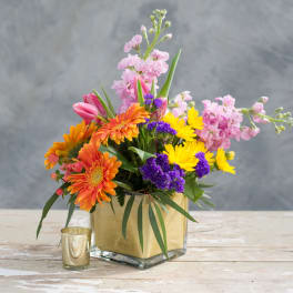 Colorful mixed bouquet in a square glass vase with a gold wrap.