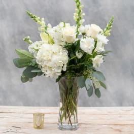 White floral bouquet in a clear glass vase with a small candle nearby