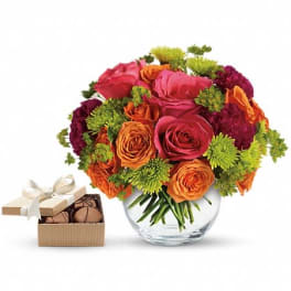 Bouquet of pink, orange, and green flowers in a glass vase with a box of chocolates