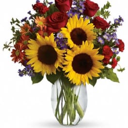 Bouquet of sunflowers, red roses, and purple daisies in a glass vase