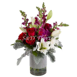 Bouquet of red roses, white lilies, and purple snapdragons in a glass vase