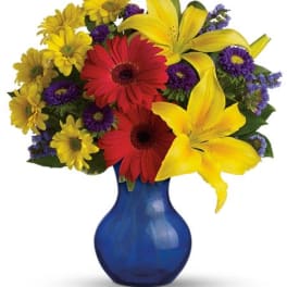 Bouquet of yellow lilies, red gerberas, and purple daisies in a blue vase