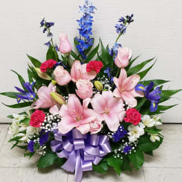 Pink lilies and roses with blue flowers in a lavender ribboned arrangement