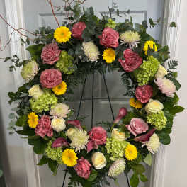 Large floral wreath with pink roses, yellow daisies, and green hydrangeas on an easel