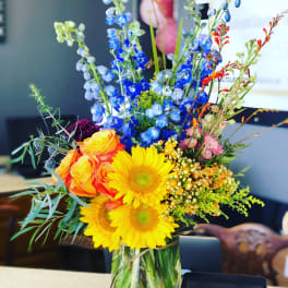 Colorful bouquet with sunflowers, roses, and blue delphinium in a glass vase