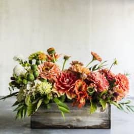 Low floral arrangement in a wooden box with orange and pink blooms