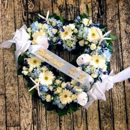 Heart-shaped floral wreath with white ribbon and pale blue flowers