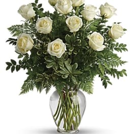 White roses arranged in a clear glass vase with dense greenery