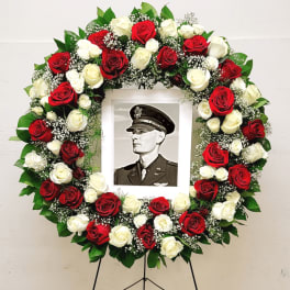 Standing wreath of red and white roses surrounding a central photo on an easel