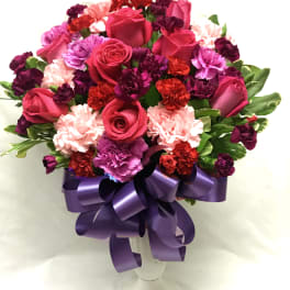 Bouquet of pink roses and carnations in a white vase with a purple ribbon