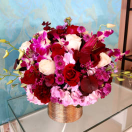 Round bouquet of red, pink, and white flowers in a gold vase