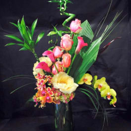 Tropical floral arrangement with pink and yellow orchids in a tall glass vase