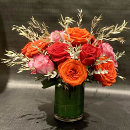 Bouquet of red, orange, and pink roses in a green glass vase