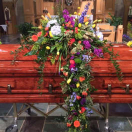 Large colorful floral cross displayed on a casket in a church