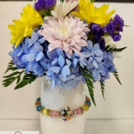 Colorful bouquet in a white vase with blue, yellow, purple, and pale pink flowers.