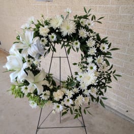 White floral wreath on a black stand with lilies and daisies