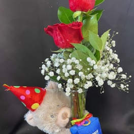 Red roses in a glass vase with a teddy bear and birthday tag