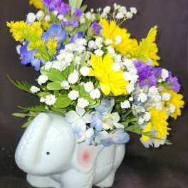 Mixed yellow, purple, white, and blue flowers in a white elephant planter