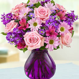 Pink roses and purple flowers in a purple glass vase