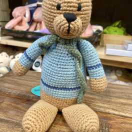 Crocheted teddy bear plush in a blue sweater sitting on a wooden surface
