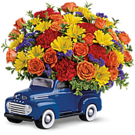 Bouquet of orange roses, yellow daisies, and red carnations in a blue truck container