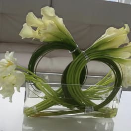 White calla lilies and white tulips arranged in a clear rectangular vase.
