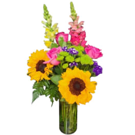 Bouquet of sunflowers, pink roses, and purple flowers in a glass vase