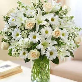 Arrangement of white lilies, daisies, and cream roses in a clear glass vase