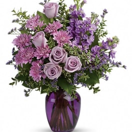 Purple roses and mixed lavender flowers in a glass vase
