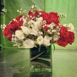 Red and white roses arranged in a square glass vase.
