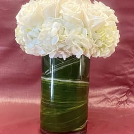 White rose and hydrangea arrangement in a tall green glass vase