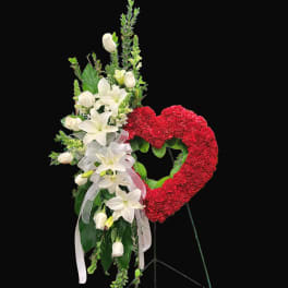 White lilies and roses beside a red heart-shaped floral wreath on a stand
