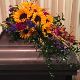 Sunflower arrangement with purple and pink flowers on a casket