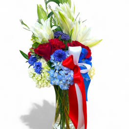 Red roses and white lilies in a glass vase with a red, white, and blue ribbon