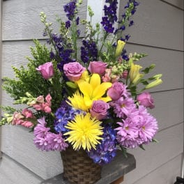 Mixed bouquet in a woven basket with pink, yellow, purple, and blue flowers