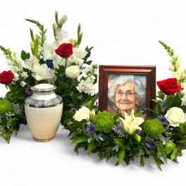 Sympathy floral tribute with framed photo and urn surrounded by red and white flowers