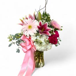 Pink and white floral arrangement in a glass vase with a pink ribbon