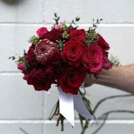 Hand-tied bouquet of red roses and burgundy blooms with a white ribbon