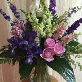 Mixed bouquet with pink roses, purple irises, and tall white and lavender spikes in a glass vase
