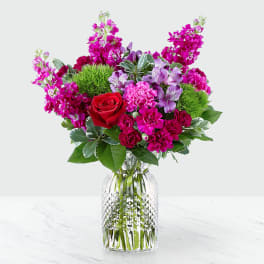 Mixed bouquet of red, pink, and purple flowers in a clear glass vase