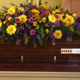 Large floral spray on a wooden casket with yellow and purple flowers