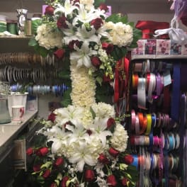 Tall floral cross with white lilies, cream roses, and red roses