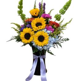 Bright mixed bouquet with sunflowers in a black vase tied with a lavender ribbon